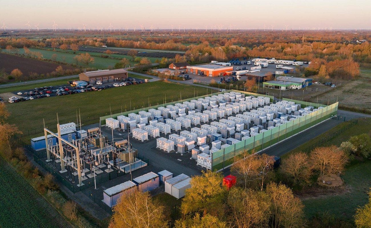 Vue aérienne d’un parc de conteneurs de batteries, éoliennes à l’horizon