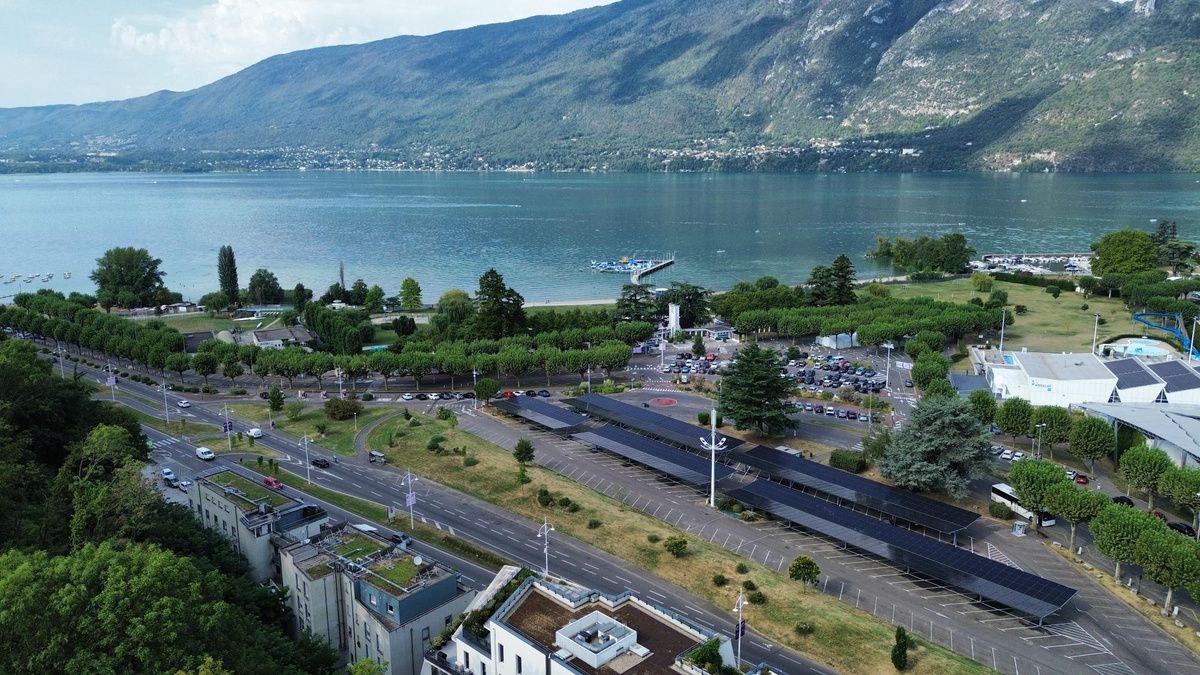 Vue aérienne d'un parking couvert d'ombrières solaires au bord d'un lac, au pied des montagnes