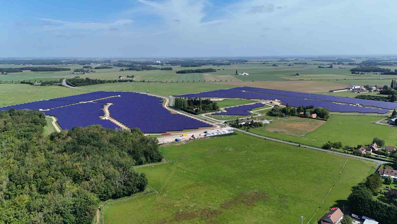 Vue aérienne d'un parc solaire au sol entouré de prairies et de bois